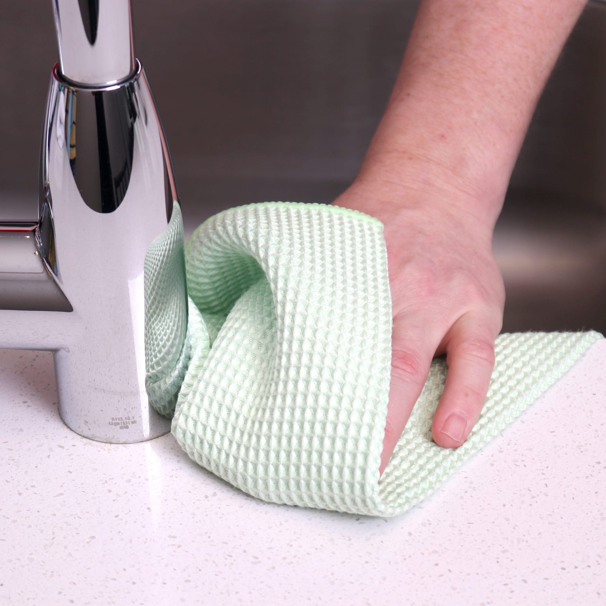 A green waffle weave towel being used by hand to clean a kitchen surface